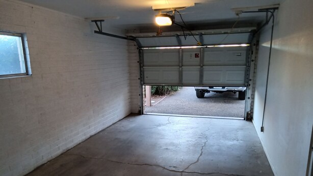 Un garage avec un sol en béton, un mur blanc et une porte de garage entrouverte.