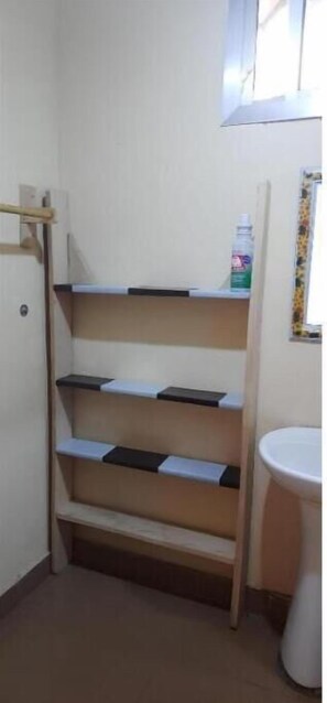 Bathroom features a pedestal sink, toilet, and storage shelf.