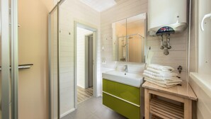 A modern bathroom with a white sink, a mirror, and a shower. There is a green cabinet below the sink and a towel rack with towels.