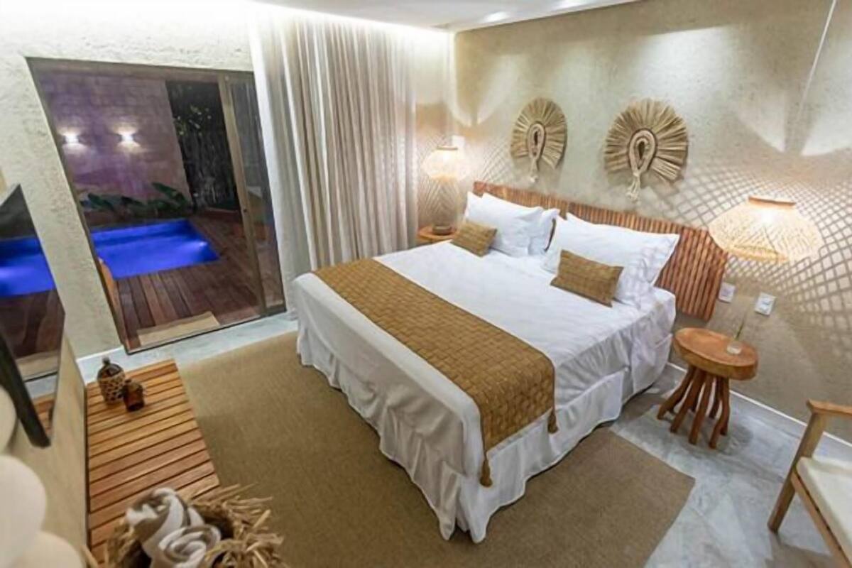 A spacious bedroom with a large bed, a wooden side table, a nightstand, and a view of an outdoor pool.