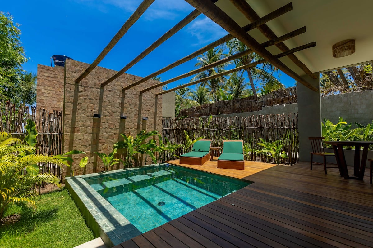 A pool area with wooden decking, lounge chairs, and a stone wall.