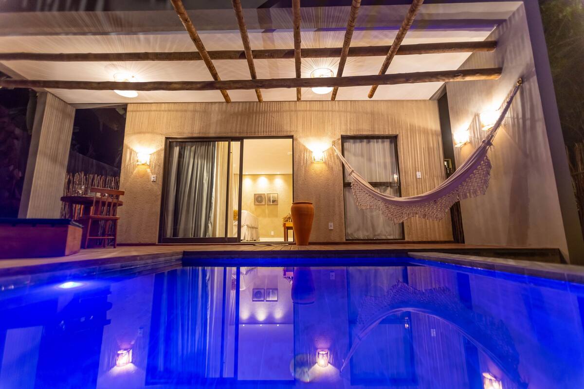 A modern hotel room with a large window, a hammock, and a pool.