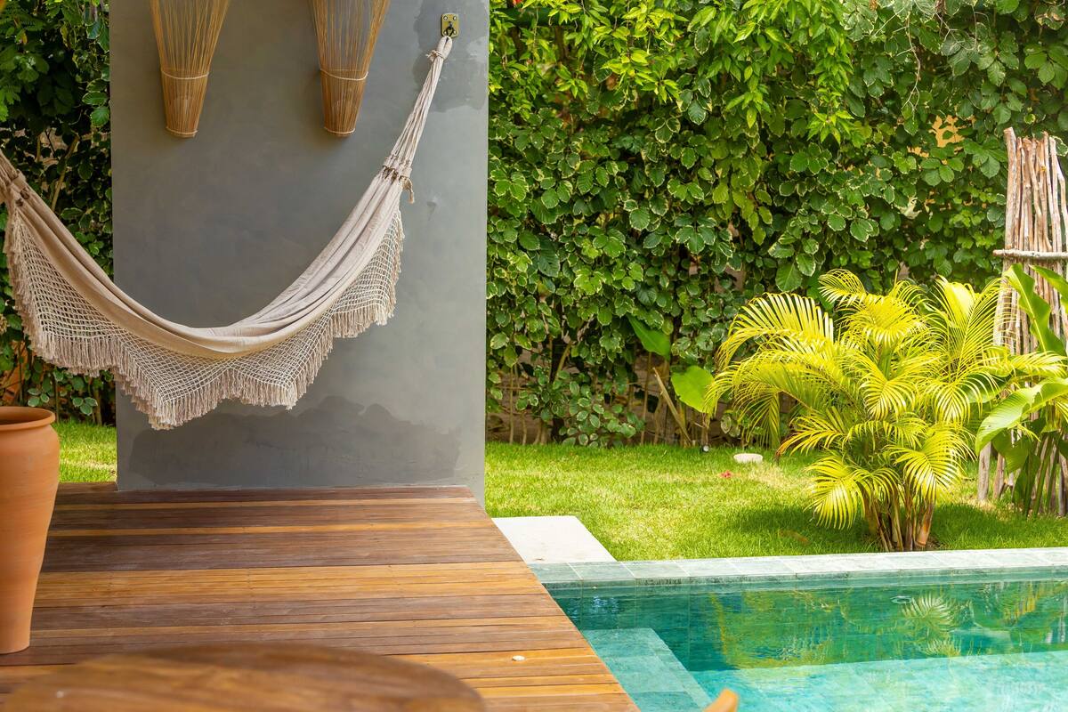 A poolside area with a hammock, a potted plant, and a lush green hedge.