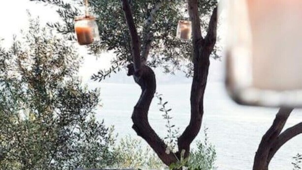 An outdoor dining area with a table set for two, overlooking a body of water, with hanging lanterns and a rustic stone wall. - White Villa (Massa Lubrense)