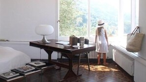 A bright room with a large window, a table with a lamp, and a child standing by the window. - White Villa (Massa Lubrense)