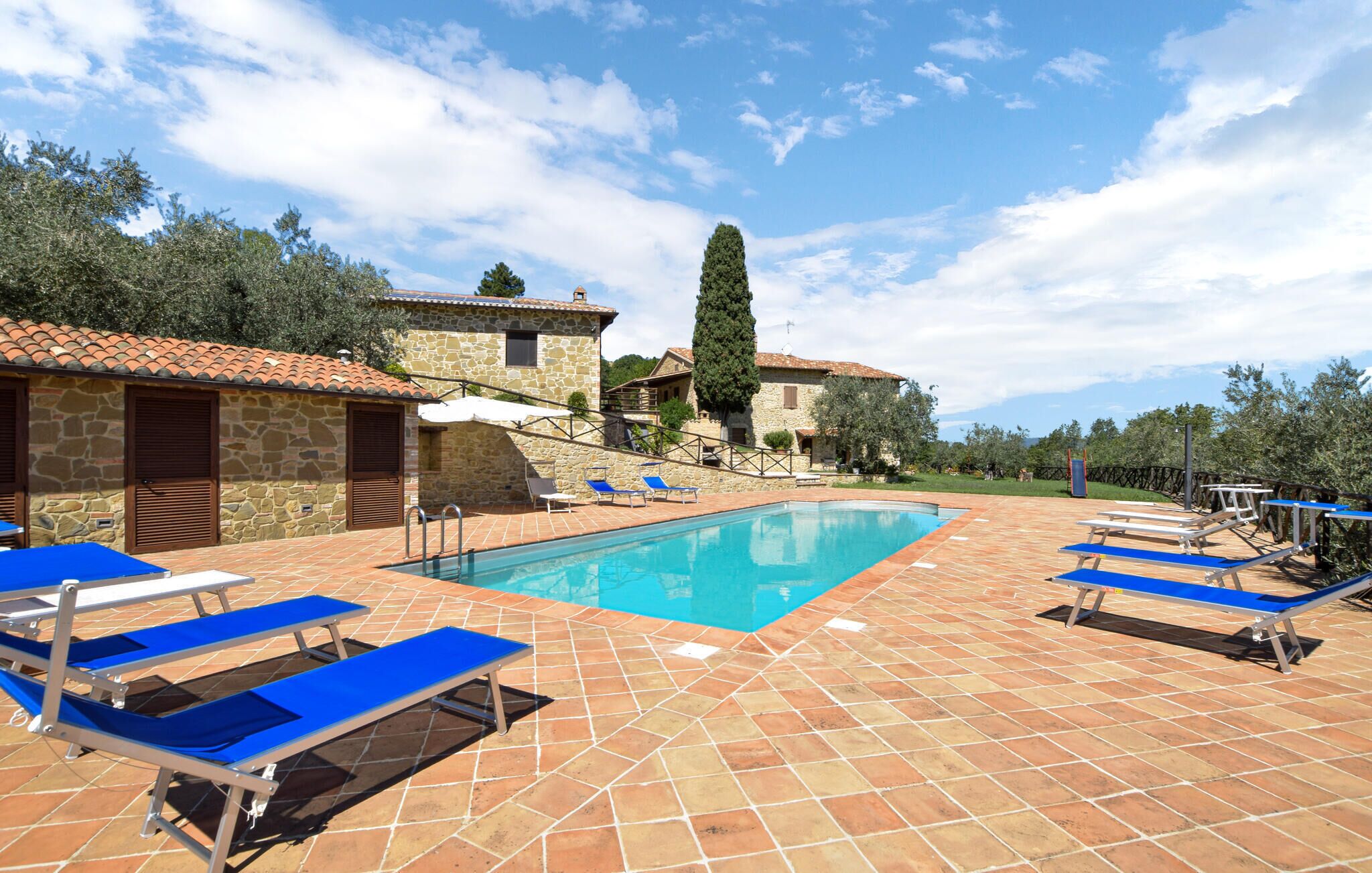 A pool area with blue lounge chairs, stone buildings, and a clear sky.