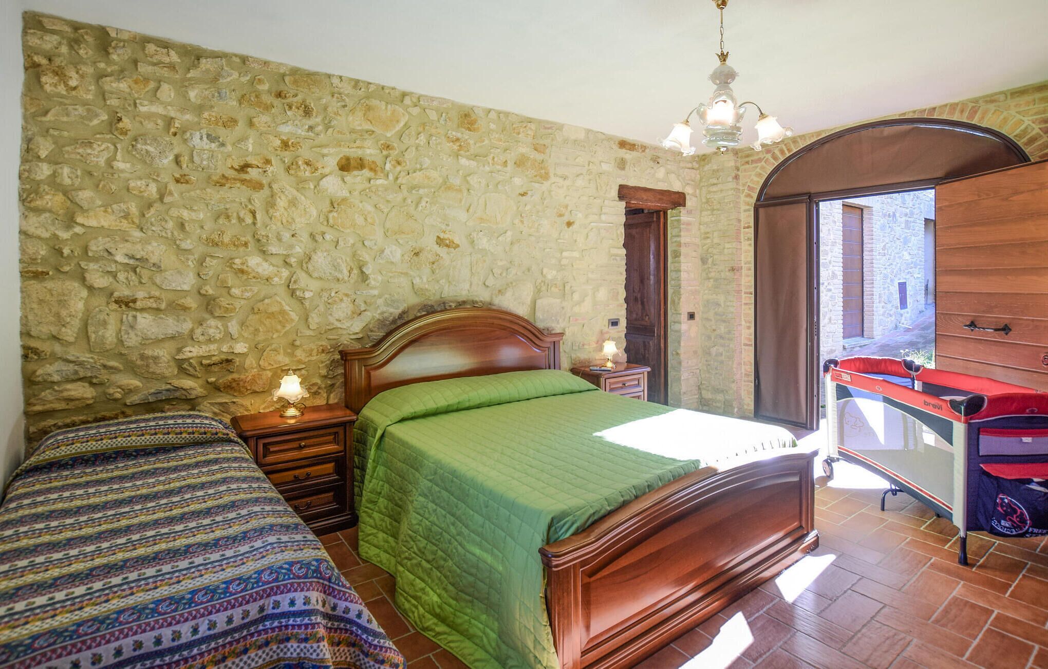 Une chambre avec un mur en pierre, un lit en bois, une table de chevet avec une lampe et une armoire.