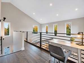 Un interior moderno con una escalera, un comedor con mesa y sillas, y ventanas amplias con vistas a follaje otoñal.