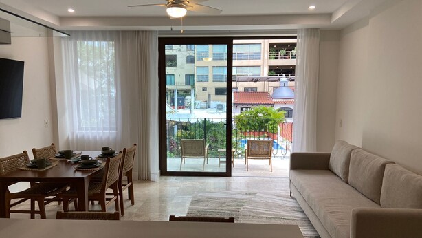 A modern living room with a dining area, a sofa, and a balcony with a view of buildings and greenery. - Francisca Luxury Suites - Adults Only (Puerto Vallarta)