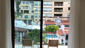 A balcony with two wicker chairs and a table, overlooking a residential area with buildings and a blue pool. - Francisca Luxury Suites - Adults Only (Puerto Vallarta)
