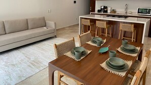 A modern kitchen with wooden cabinets, a dining table set with green plates and bowls, and a beige sofa in the living area. - Francisca Luxury Suites - Adults Only (Puerto Vallarta)
