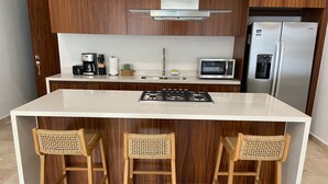 A modern kitchen with a central island, two bar stools, a microwave, a coffee maker, and a refrigerator. - Francisca Luxury Suites - Adults Only (Puerto Vallarta)