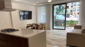 A modern kitchen with a gas stove, a dining area with wooden chairs, a sofa, and a large sliding glass door leading to a balcony with a view of buildings. - Francisca Luxury Suites - Adults Only (Puerto Vallarta)