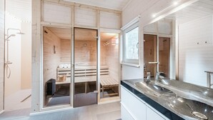 Et moderne badeværelse med en træsauna, et stort spejl og en vask med bordplade.