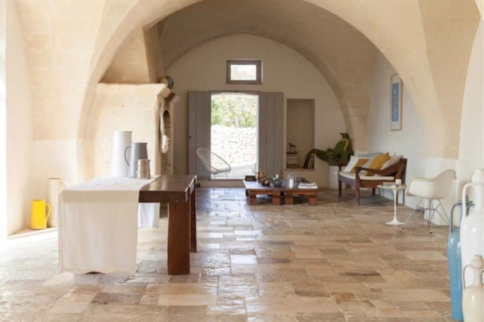 An arched hallway with a stone floor, a wooden table, and a seating area with a sofa and chairs.