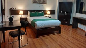 A hotel room with a bed, two bedside tables with lamps, a desk with a chair, a potted plant, a large mirror, a wardrobe, and a wall-mounted artwork. - Hotel Tu luz Arequipa (Arequipa)