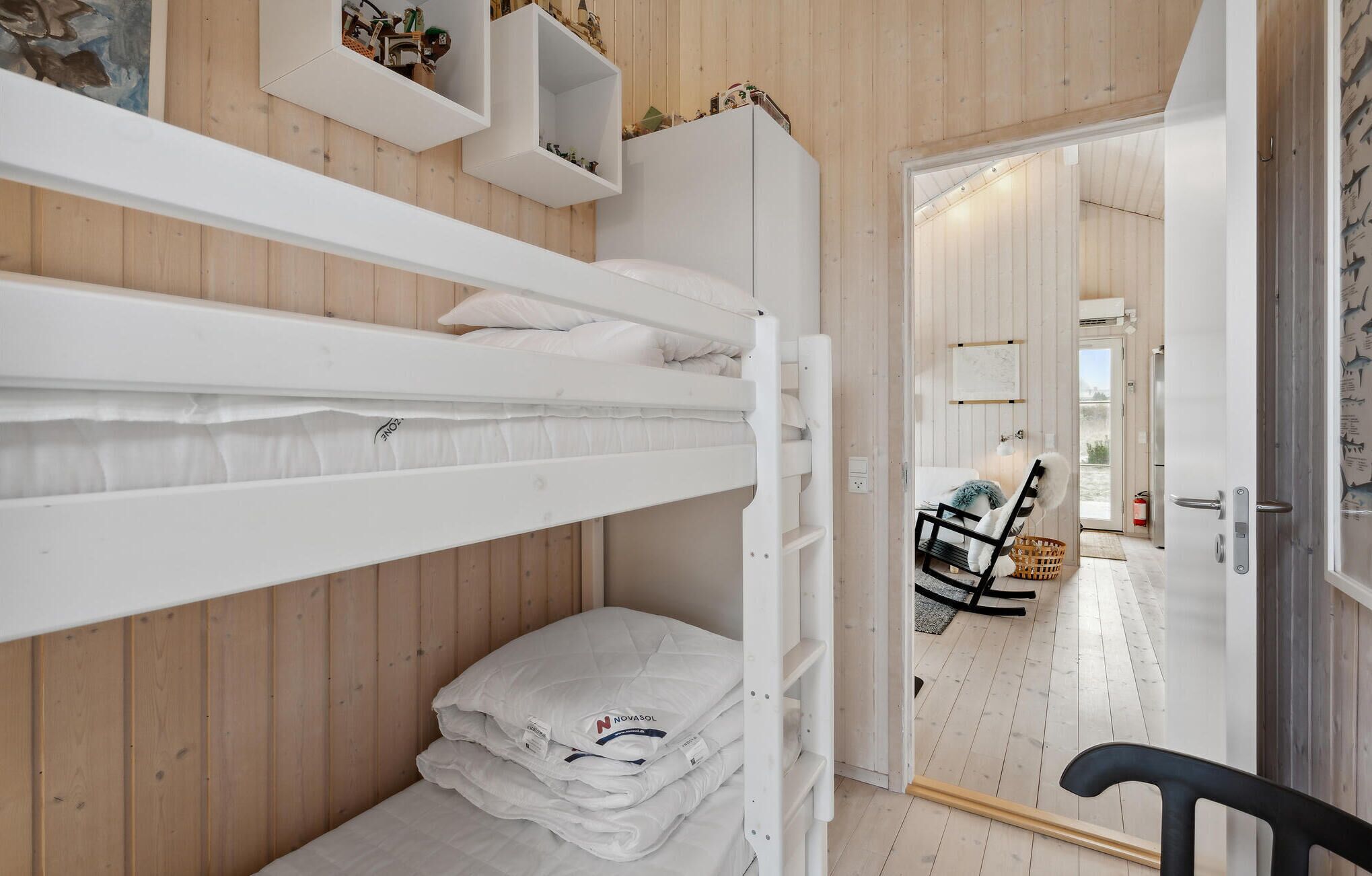 A bunk bed room with wooden walls, a white door, and a view into another room with a chair and a basket.