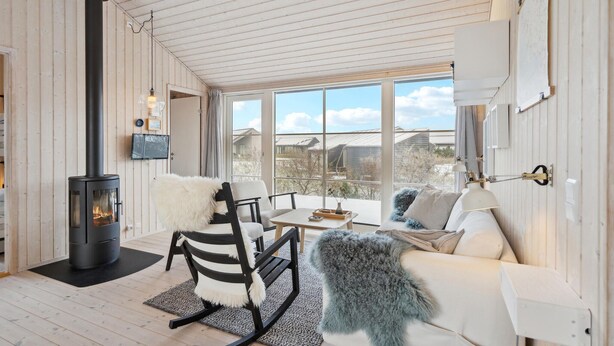 A cozy room with a wood-burning stove, a sofa, a rocking chair, and a large window offering a view of the outside. - 3 bedroom cozy home in Lundby (Lundby)