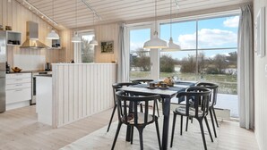 A modern kitchen with wooden paneling, a dining area with black chairs, and large windows offering a view of the outdoors. - 3 bedroom cozy home in Lundby (Lundby)