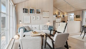 A modern living room with a white sofa, two armchairs, a coffee table, and a fireplace. There are bookshelves with books and decorative items on the wall. - 3 bedroom cozy home in Lundby (Lundby)