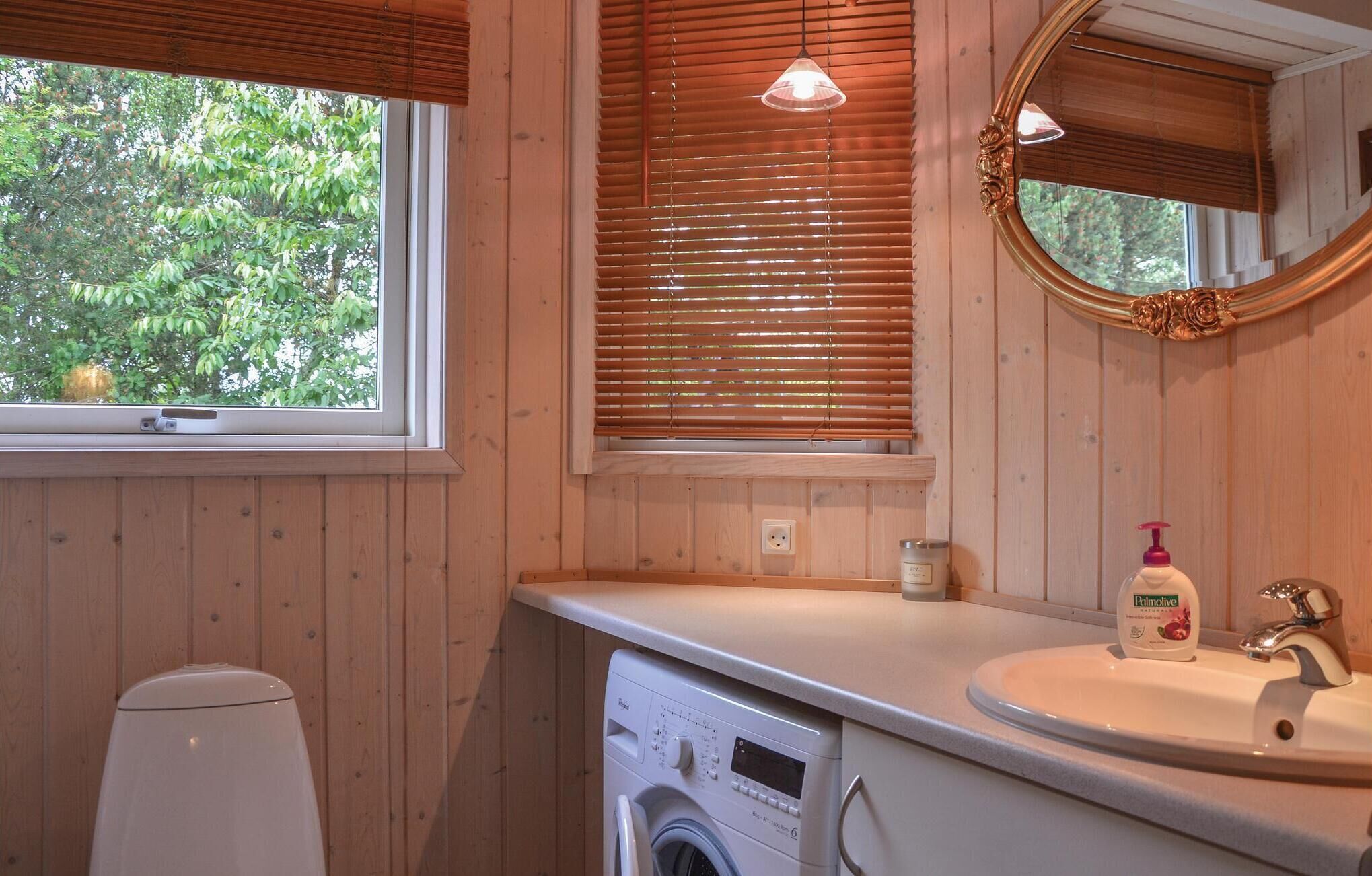 Un baño con paredes de madera, una lavadora, un lavamanos con espejo y una ventana con persianas.