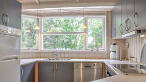 Moderni keittiö, jossa on suuri ikkuna, ruostumattomasta teräksestä valmistetut kodinkoneet ja puiset keittiökaapit.