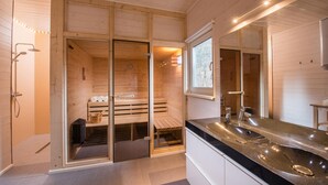 Una sauna in legno moderna con porta in vetro, un lavandino e uno specchio in un ambiente ben illuminato.