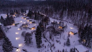 Una foresta innevata con diverse baite, ognuna con finestre e luci visibili, che suggeriscono una zona di alloggio accogliente e rustica.