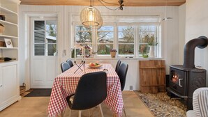 A cozy dining area with a checkered tablecloth, wooden chairs, a hanging light fixture, and a wood-burning stove. - Cozy home in Haderslev with WiFi (Haderslev)