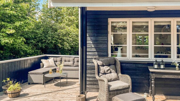 A covered outdoor patio with wicker furniture, a built-in seating area, and a window overlooking greenery. - Cozy home in Haderslev with WiFi (Haderslev)