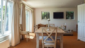 A dining area with a wooden table and chairs, a glass coffee table, and a view of the outdoors through large windows. - 3 bedroom accommodation in Gorran Haven (Gorran Haven)