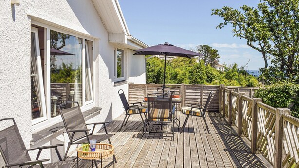 A wooden deck with outdoor furniture, including chairs and a table, and a large umbrella providing shade. - 3 bedroom accommodation in Gorran Haven (Gorran Haven)