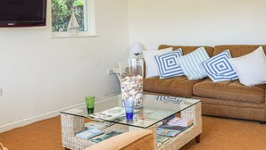 A living room with a brown sofa, a glass coffee table with magazines, and a decorative vase with seashells. - 3 bedroom accommodation in Gorran Haven (Gorran Haven)