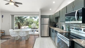 Une cuisine moderne équipée d’un réfrigérateur en acier inoxydable, d’un four encastré et d’un four à micro-ondes. On y trouve également un coin repas avec des chaises blanches et une table.