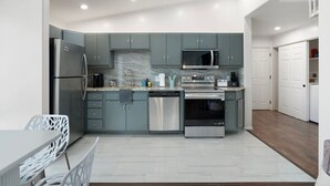 Une cuisine moderne avec des meubles gris, des appareils en acier inoxydable et un pare-feu en marbre.