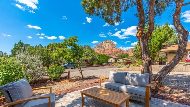 Un espace extérieur aménagé avec une table en bois et deux chaises en osier, entouré d’arbres et offrant une vue sur une montagne.