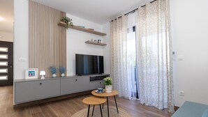 Een moderne woonkamer met een televisie, grijze kasten, een klein tafeltje en een gordijn met een patroon.