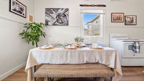 A dining table set with plates, glasses, and a plant, in a room with a stove and framed pictures on the wall. - Midtown Flight Deck: 2BR Gem (Reno)