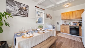 A dining area with a table set for four, a kitchen with wooden cabinets, and a large airplane painting on the wall. - Midtown Flight Deck: 2BR Gem (Reno)