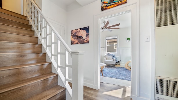 A wooden staircase with white railings leading to a room with a ceiling fan, a painting, and a view of a blue carpeted area. - Midtown Flight Deck: 2BR Gem (Reno)