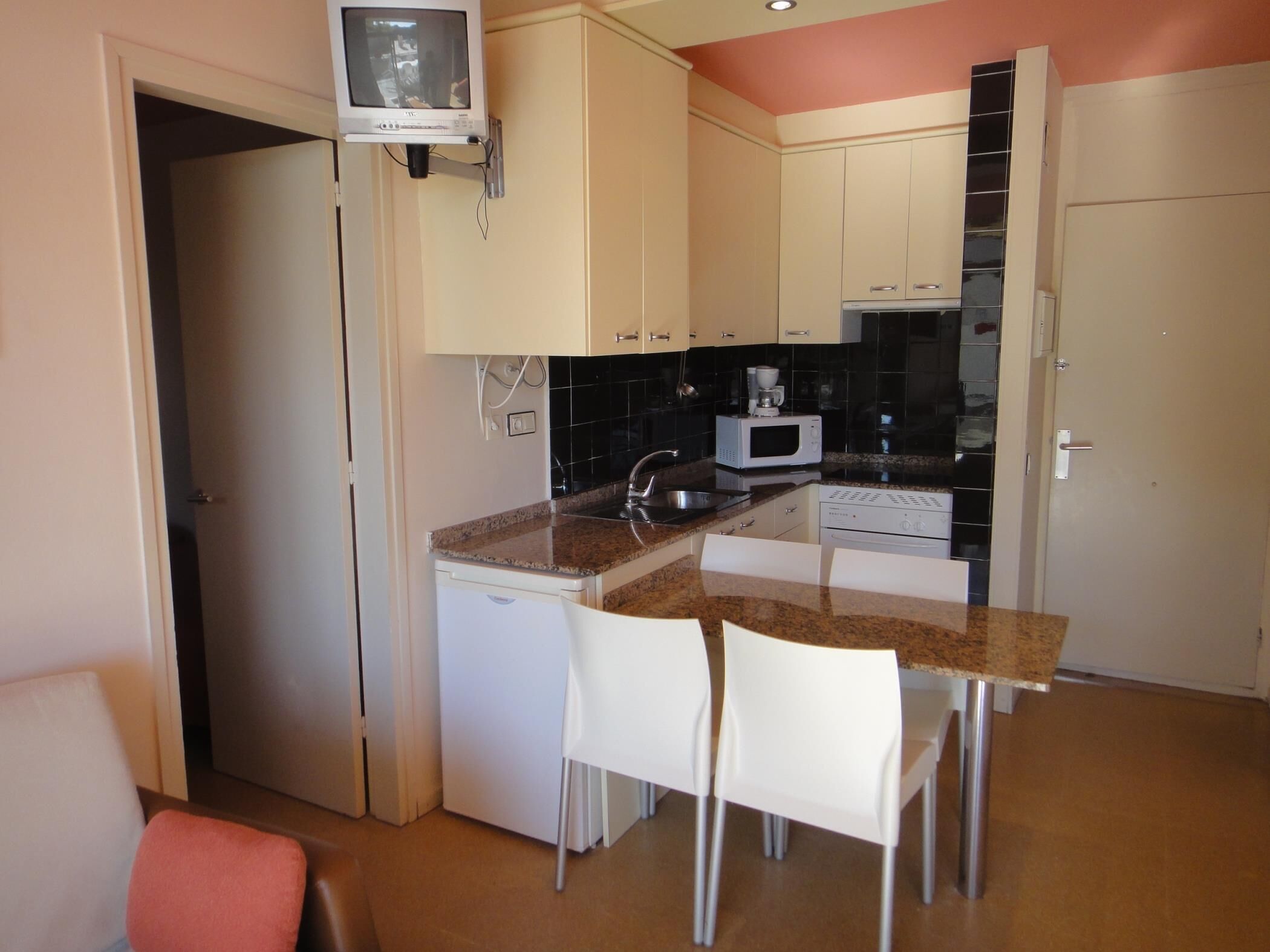 A compact kitchen with a microwave, stove, and a small television mounted on the wall.
