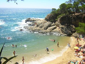 A beach with rocky cliffs, clear blue water, and people enjoying the sun and sea.