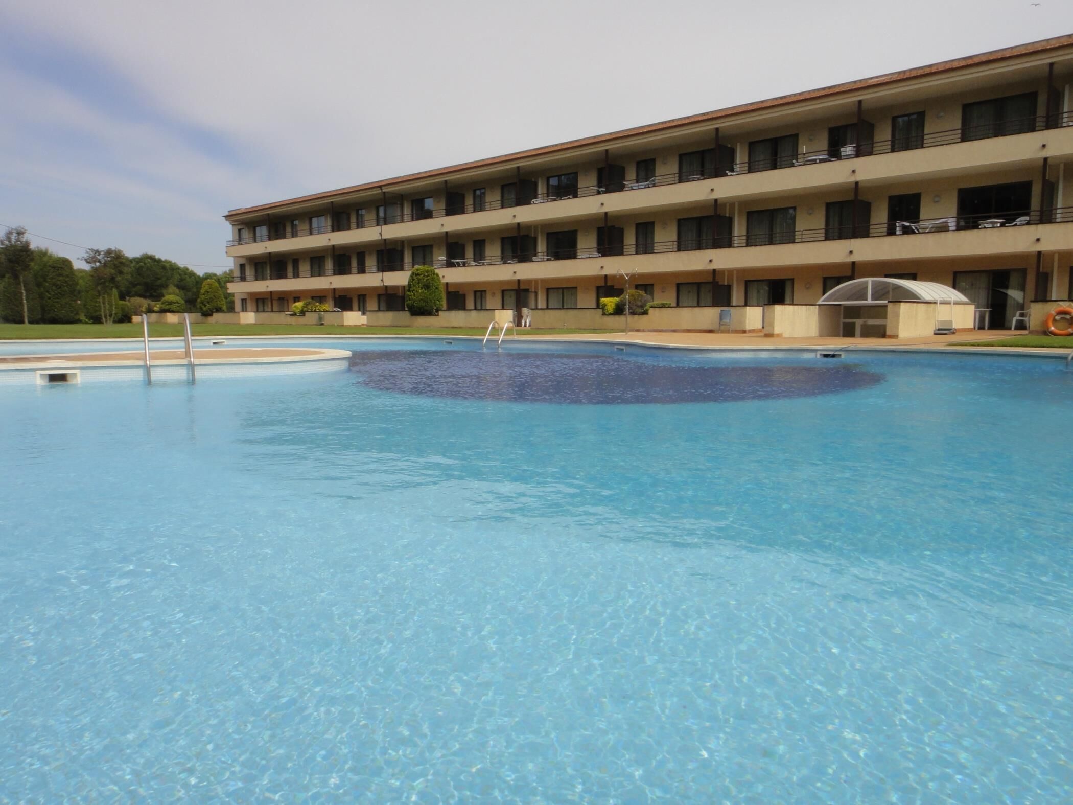 A hotel with a large swimming pool, multiple balconies, and a covered area.