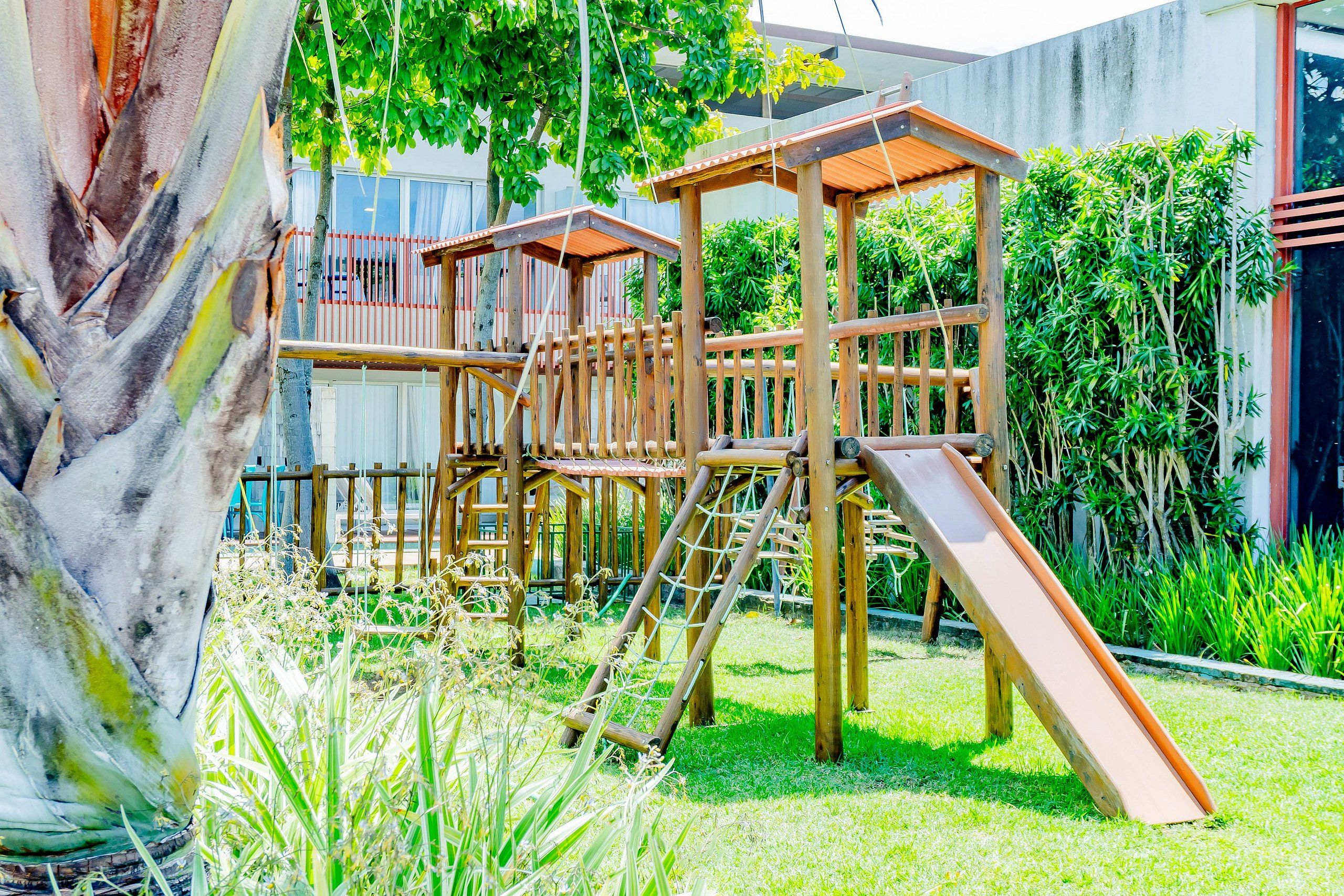 Estructura de juego de madera con un tobogán en un patio trasero cubierto de césped.