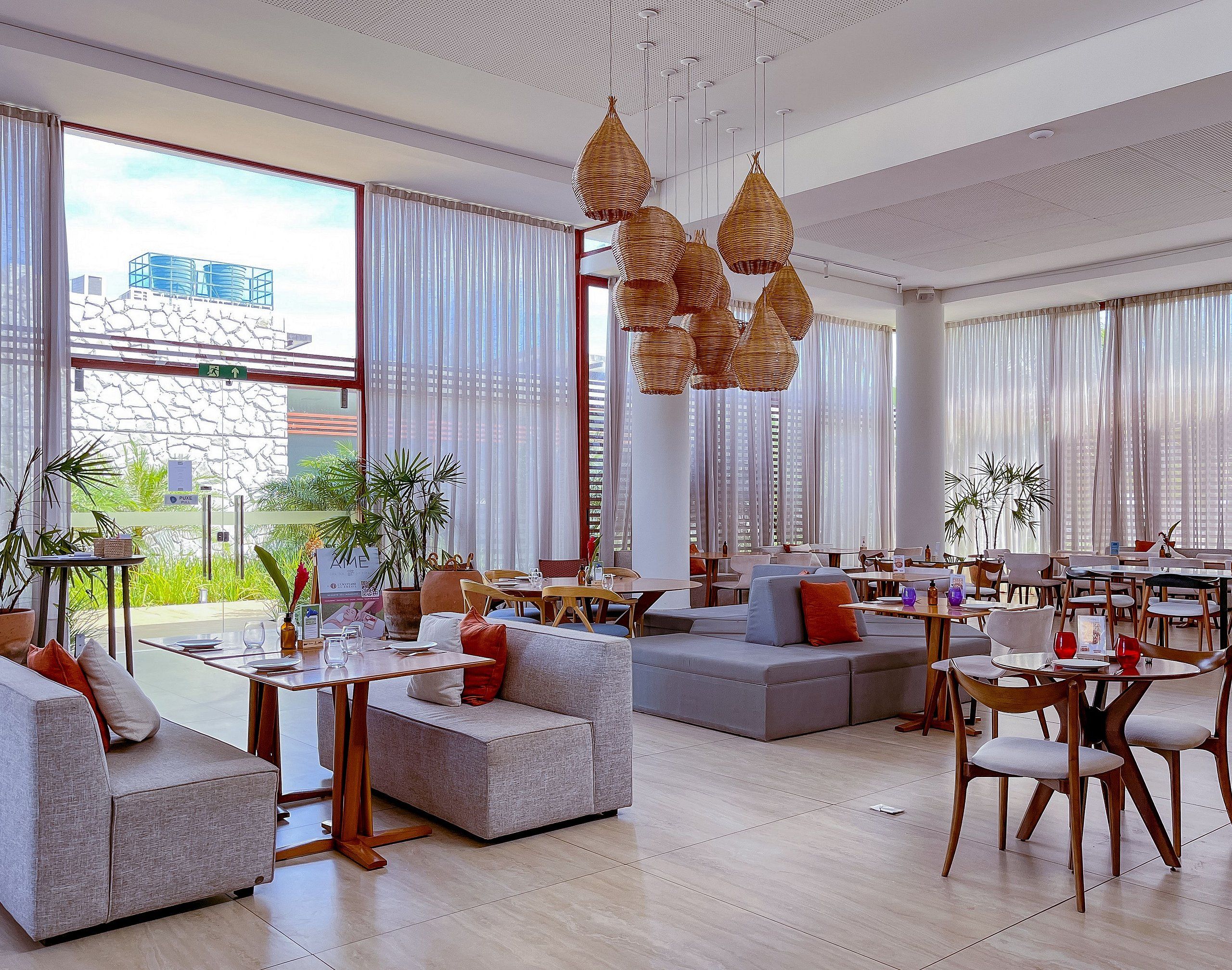 Um saguão de hotel moderno com áreas de estar, janelas amplas e luminárias de vime suspensas.