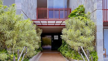 Una entrada de edificio moderna con un sendero de madera, barandas de metal y una barandilla de balcón roja.