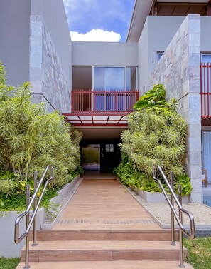 A modern building entrance with a wooden pathway, metal railings, and a red balcony railing. - Ile de Pipa- Summer Pipa (Tibau do Sul)