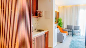 Una cocina moderna con lavamanos y armarios, un comedor con sofá y sillones, y una sala de estar con sofá y una planta.