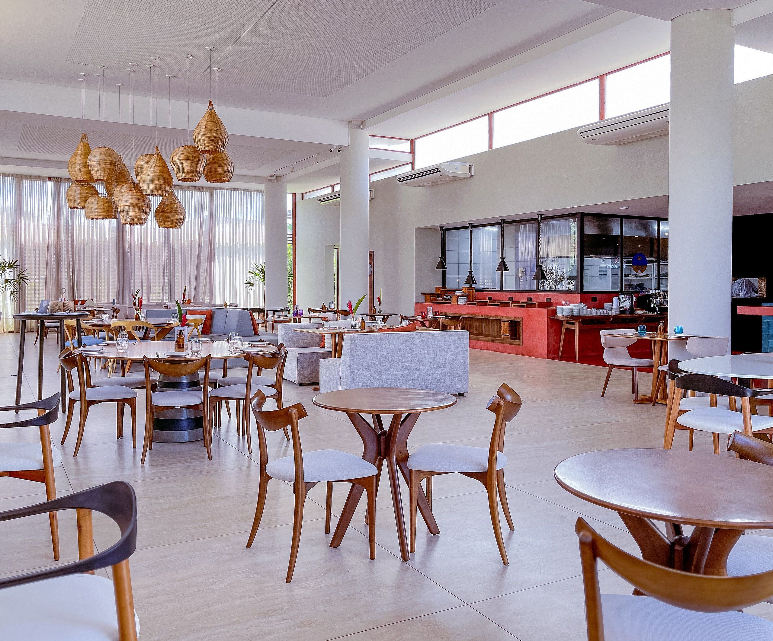 Un lobby espacioso de hotel con varias zonas de estar, un bar central y grandes ventanales que dejan entrar luz natural.