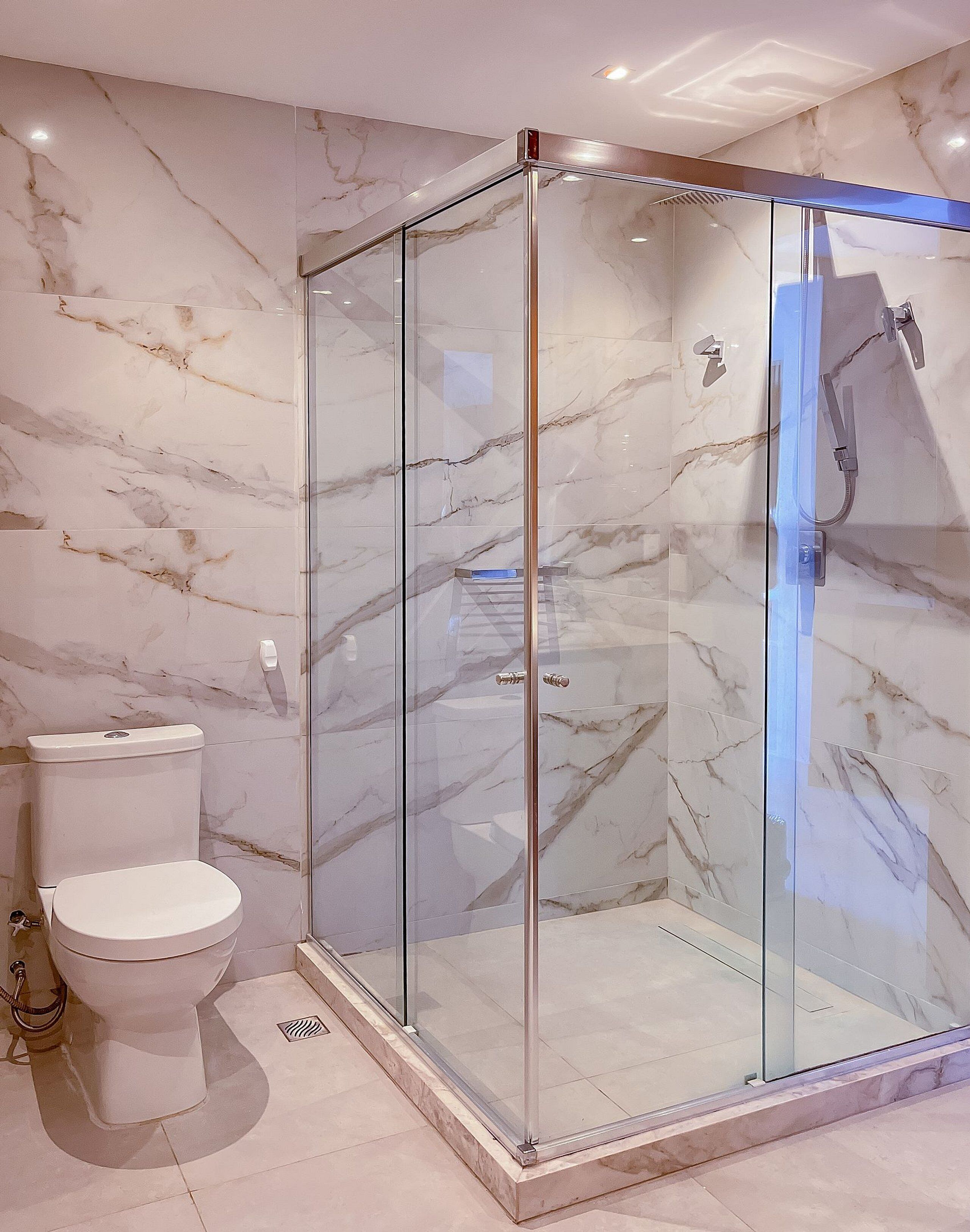 Un baño con ducha separada por mampara de vidrio, inodoro y paredes de mármol.